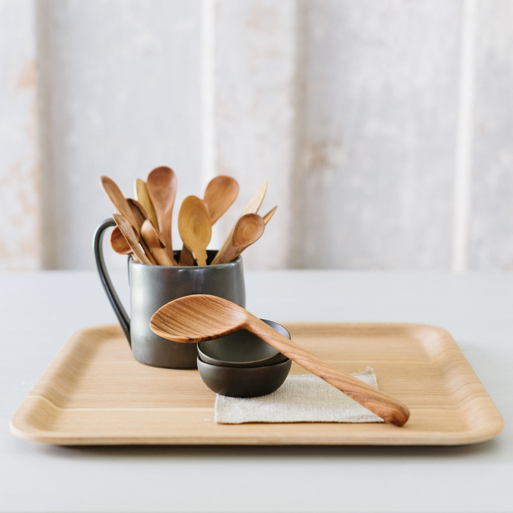 A set of wooden kitchen utensils, including a la wooden spoon, on a tray with a grey coaster