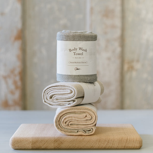 A stack of folded beige and gray towels on a wooden surface with a container of body wash on top, all against a textured wall.