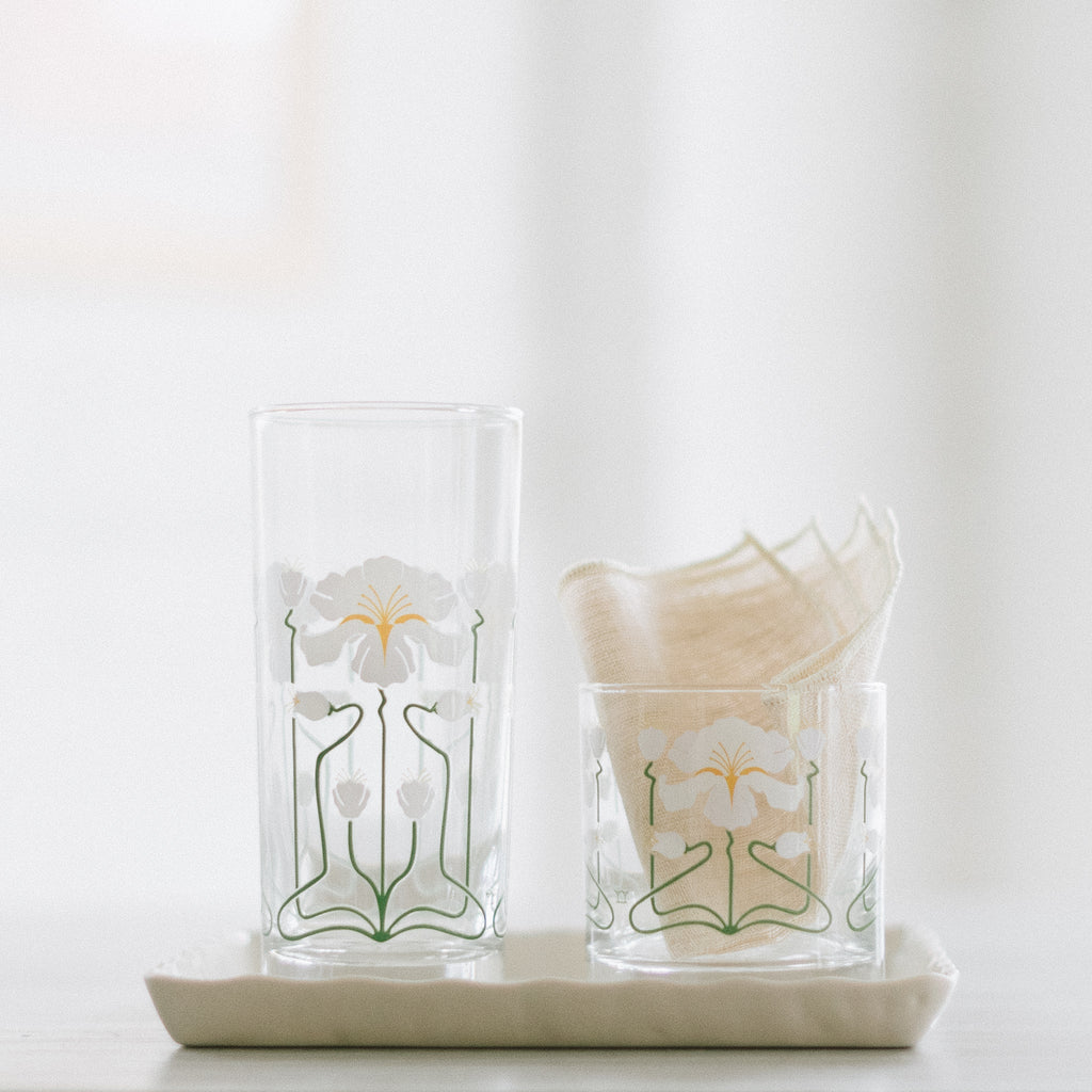 Two glasses with white irises wrapped around the glasses. They are set on a ceramic dish. One of the glasses has a cocktail napkin in it. 