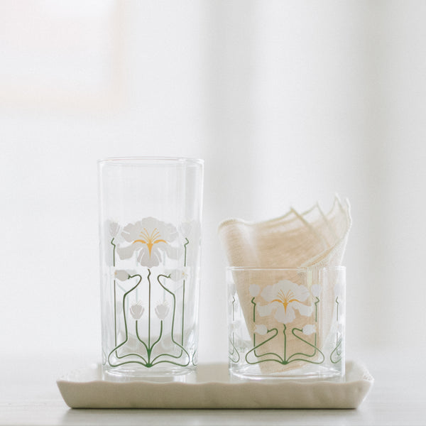 Two glasses with white irises wrapped around the glasses. They are set on a ceramic dish. One of the glasses has a cocktail napkin in it. 