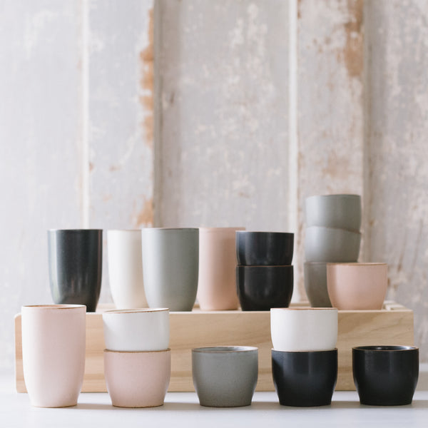 A collection of NORI tumblers in various shades of beige, gray, black, and pink, arranged in rows on a wooden surface.