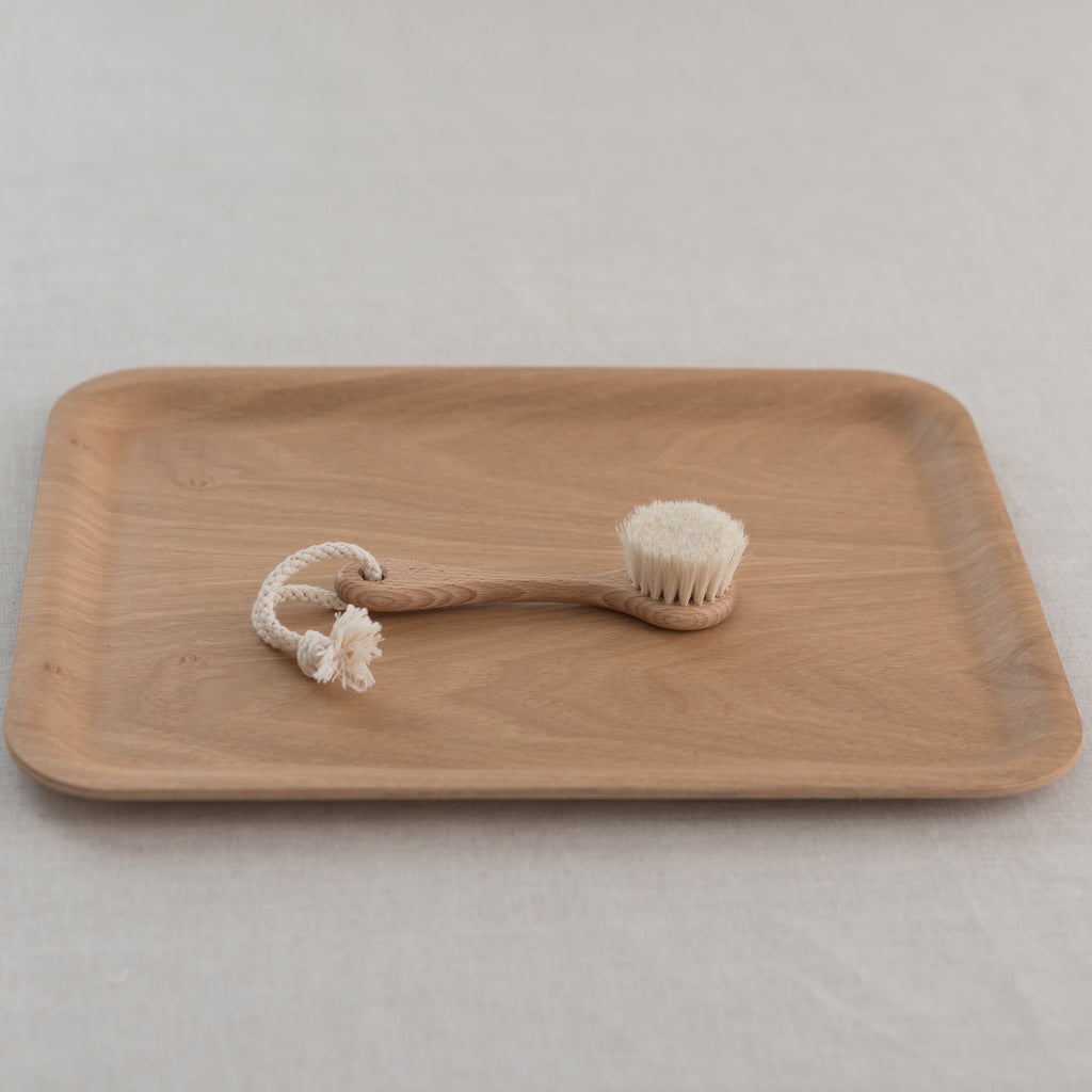 A beige wooden face brush with goat hair bristles, displayed on a wooden surface with a white background.