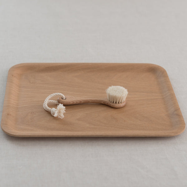 A beige wooden face brush with goat hair bristles, displayed on a wooden surface with a white background.