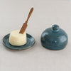 Wooden knife in butter on a blue ceramics butterdish. Next to the butter is the top/dome matching the butter dish