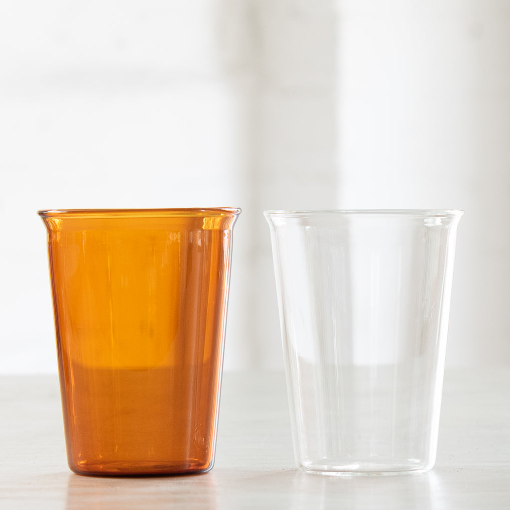 Two tall drinking glasses, one amber and one clear glass.