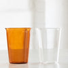 Two tall drinking glasses, one amber and one clear glass.