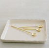 three gold spoons on a white ceramic tray