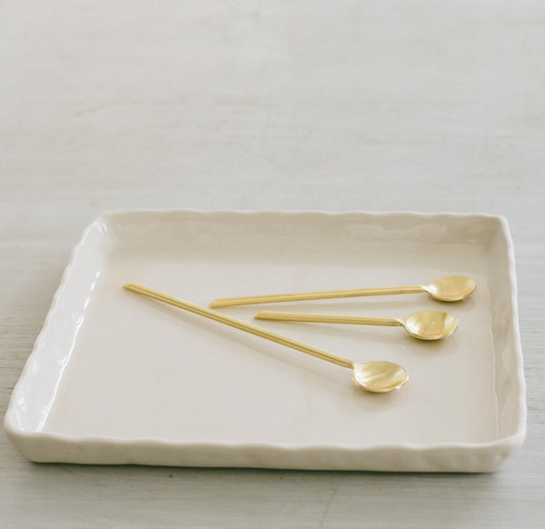 three gold spoons on a white ceramic tray