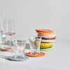 Handmade wool coasters in various natural colors placed on a white surface with two glasses of different sizes.